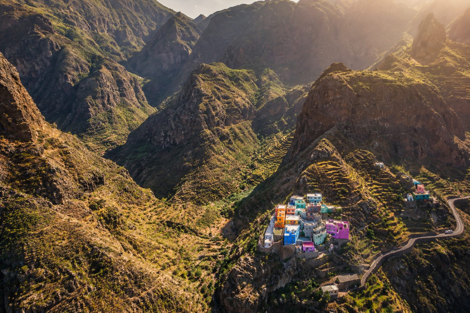 A cluster of brightly painted houses on a ridge among the green mountains and terraces of Santo Antão, Cape Verde