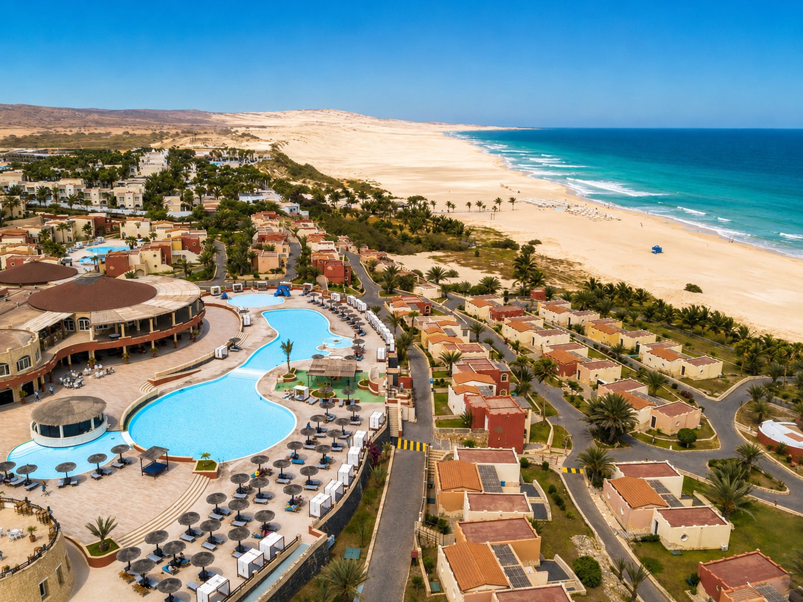 A beachfront restaurant with palm trees, sun umbrellas and a painted boat on the sand, Cape Verde