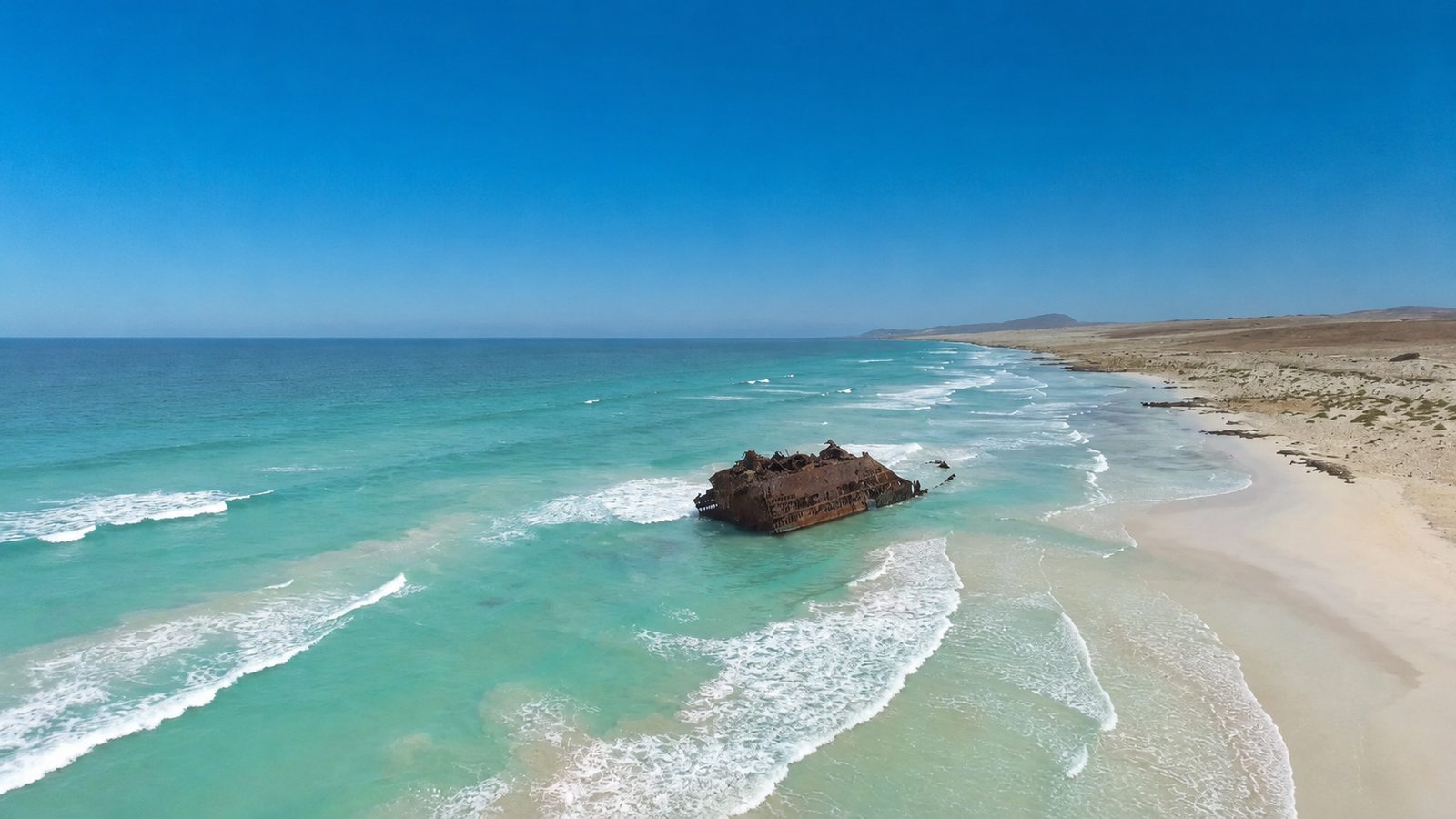 The rusting hull of the Cabo Santa Maria shipwreck standing in breaking surf off an empty stretch of coast on Boa Vista