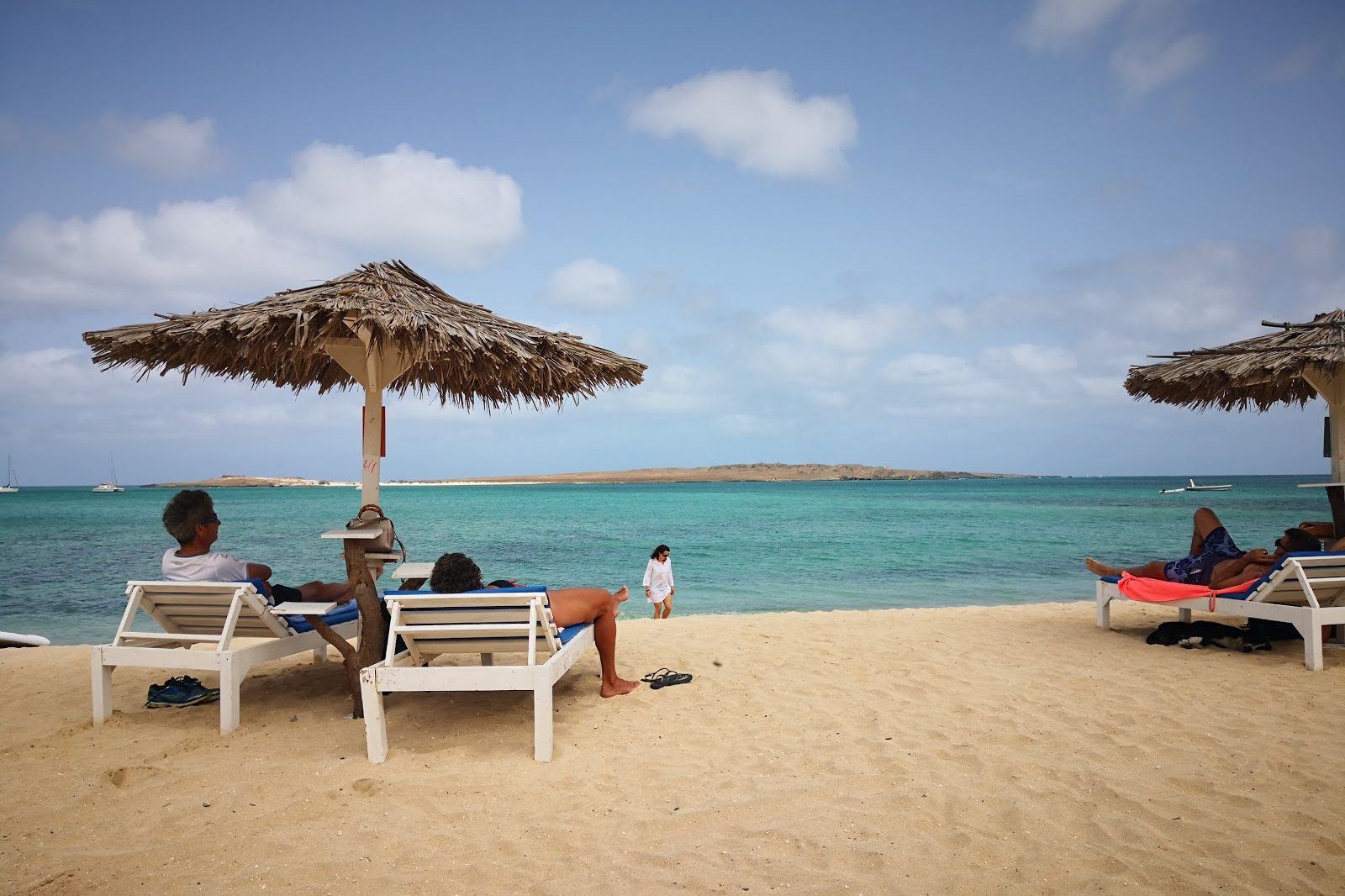 Thatched sun umbrellas and loungers on the sand at Praia de Cabral, Boa Vista, with calm turquoise water and the low offshore islet behind