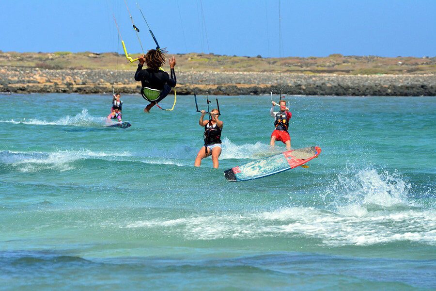 Four kitesurfers riding close to shore off Praia do Estoril, Boa Vista, with the low rocky coastline behind them