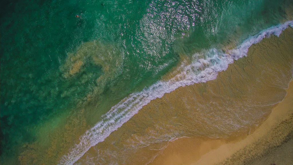 Aerial view of a shore break folding onto a steep sand beach on Boa Vista, with churned water showing where the sand shelves away