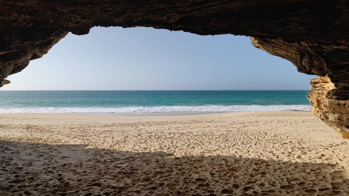 View out through a sea cave at Varandinha on the west coast of Boa Vista, framing empty sand and Atlantic surf