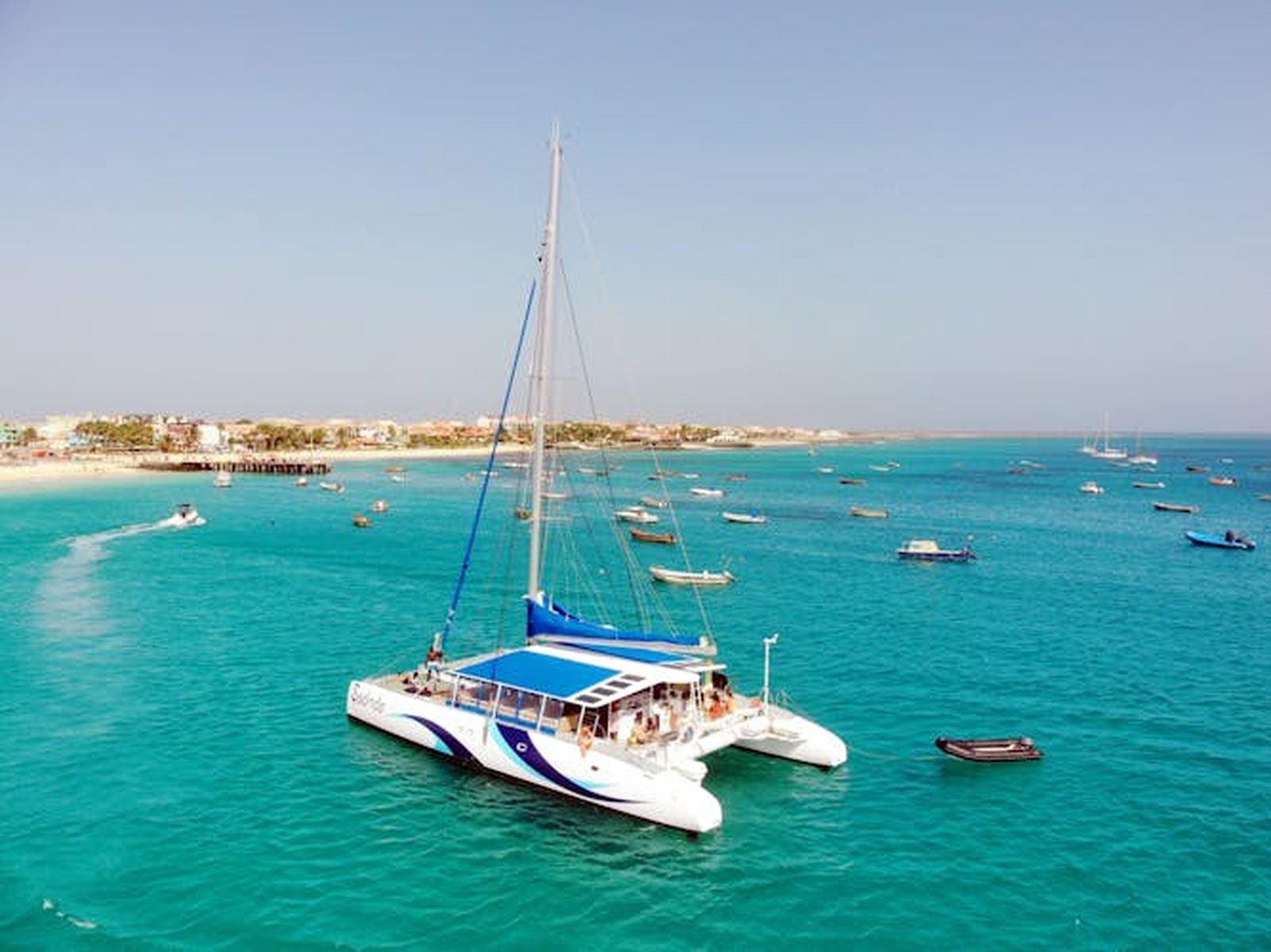 A catamaran moored in the turquoise bay off Santa Maria on Sal, with boats and the town behind, Cape Verde