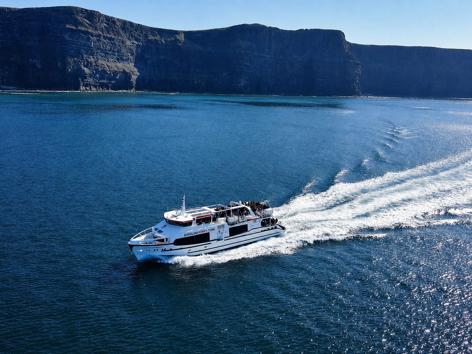 A passenger ferry crossing open water beneath tall sea cliffs