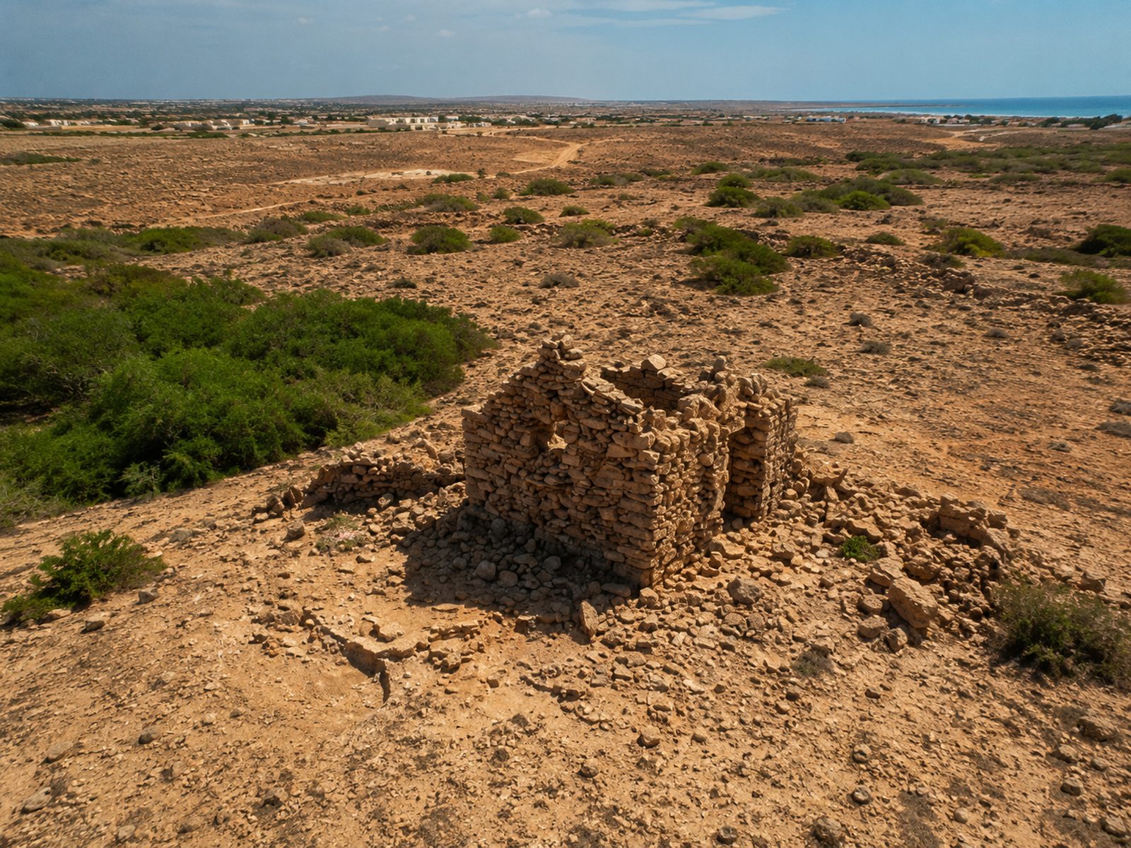 Stone ruins of the abandoned village of Curral Velho in the dry scrubland of southern Boa Vista, with the sea beyond, Cape Verde
