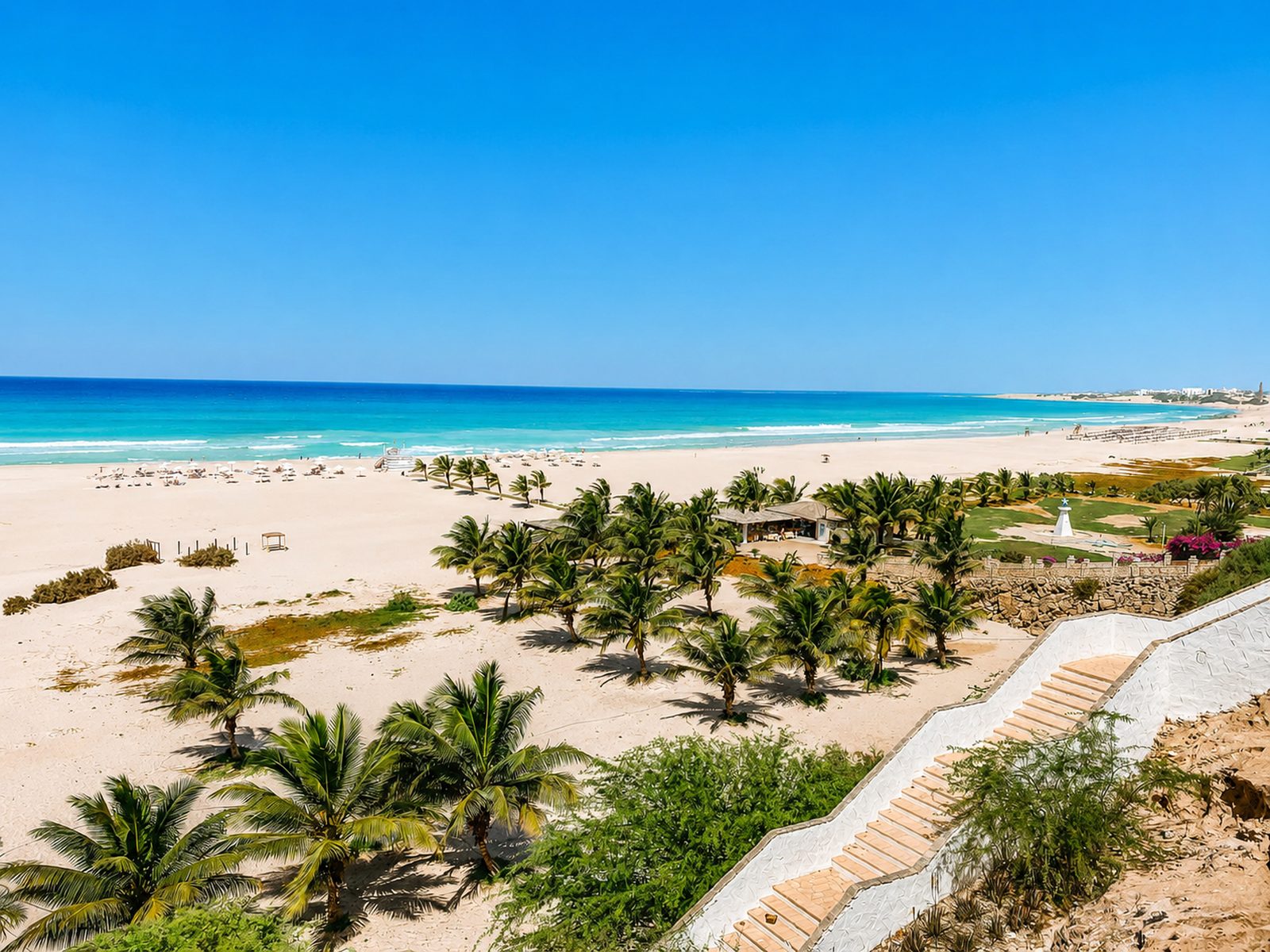 A tall sculpture of recycled bottles on a Cape Verdean beach with palm trees under a blue sky