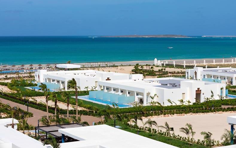 Riu Palace Boavista on Boa Vista, Cape Verde: white low-rise buildings and palm gardens above the beach, with an islet offshore