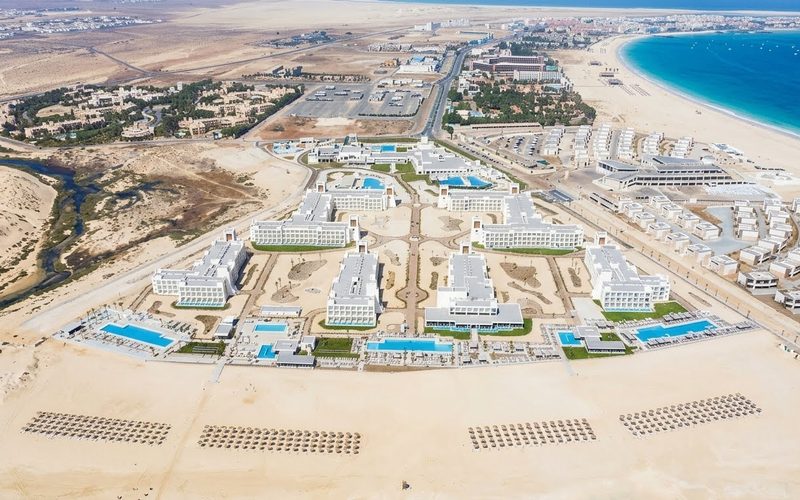 Aerial view of Riu Palace Santa Maria on Sal, Cape Verde: white hotel blocks and pools behind a wide sandy beach, with Santa Maria bay in the distance