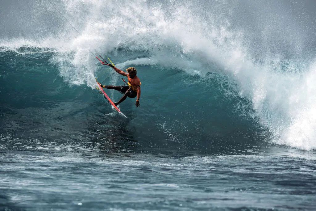 A kitesurfer carving through the face of a large breaking wave in open water off Sal, Cape Verde