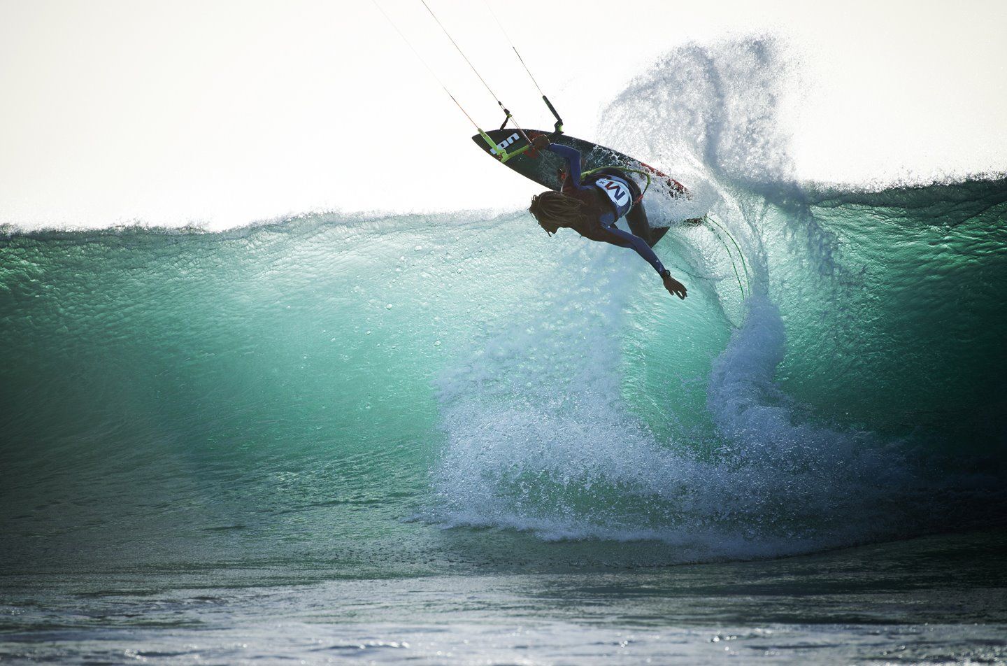A kitesurfer driving off the lip of a large green wave off Sal, Cape Verde, with spray blowing back from the crest