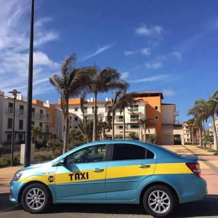 A turquoise and yellow taxi parked on a palm-lined street beside apartment blocks in Santa Maria, Sal