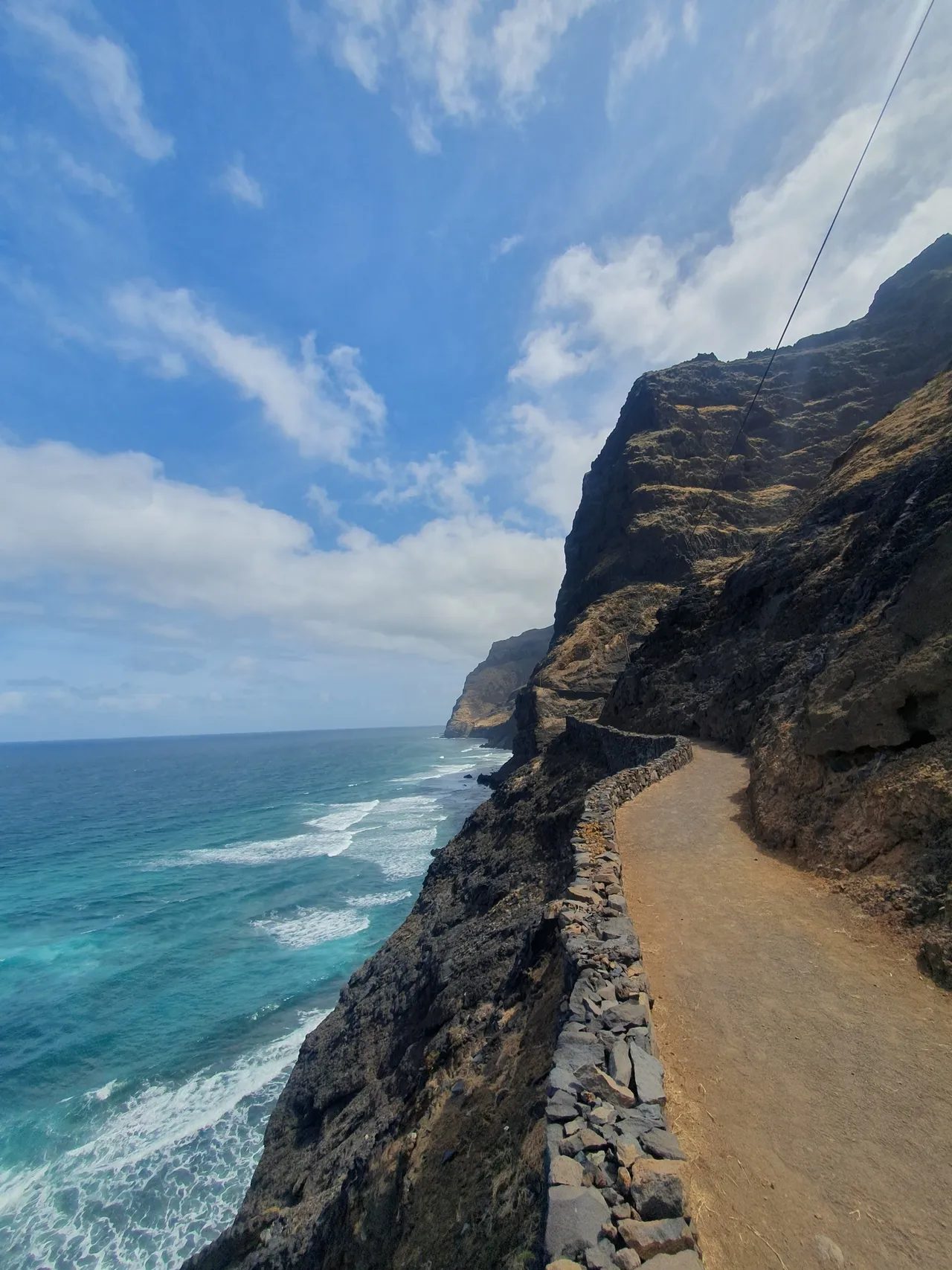 Earth path with a low stone wall running along a sheer sea cliff on the Cruzinha coastal path, Santo Antão