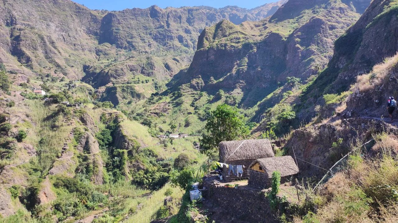 Traditional stone houses with thatched roofs on a hillside path above a deep green valley, Santo Antão