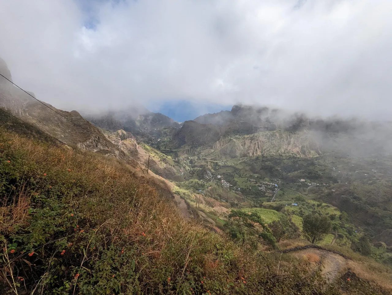 Grassy hillside path above the Paul Valley, with villages below and low cloud over the mountains, Santo Antão