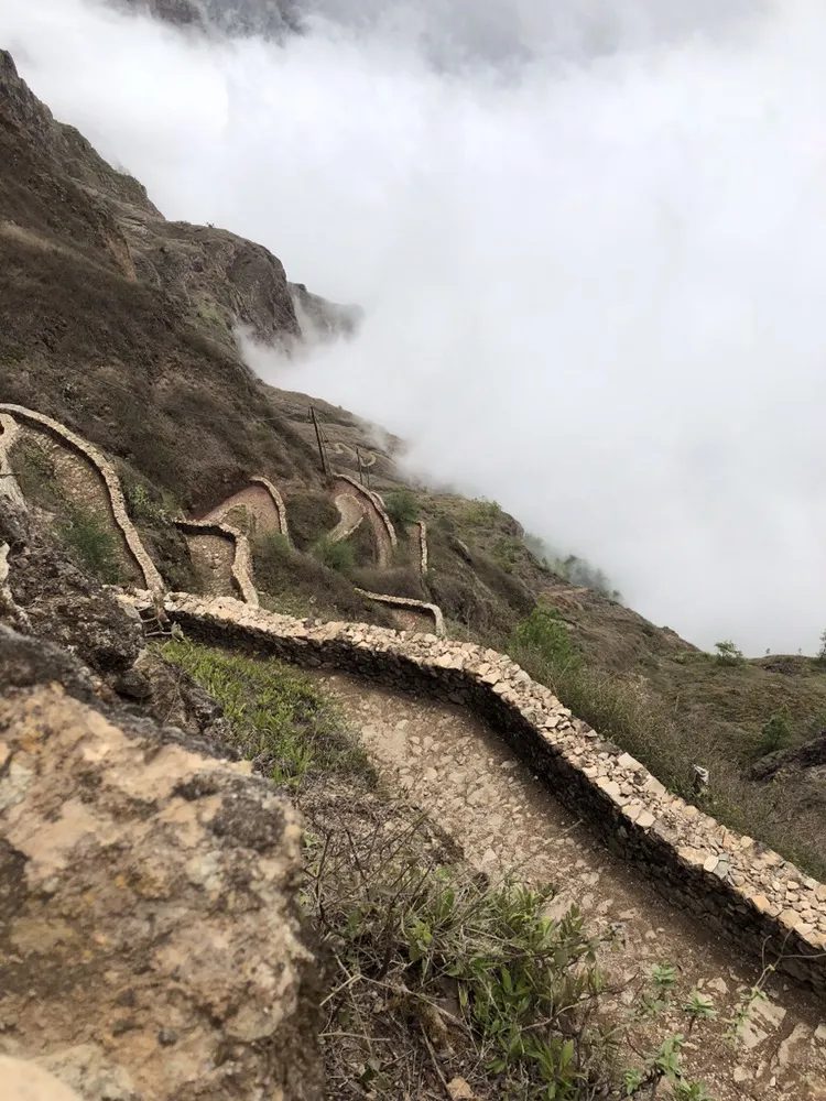 Stone-walled cobbled path zigzagging down a steep mountainside into cloud below the Cova crater rim, Santo Antão