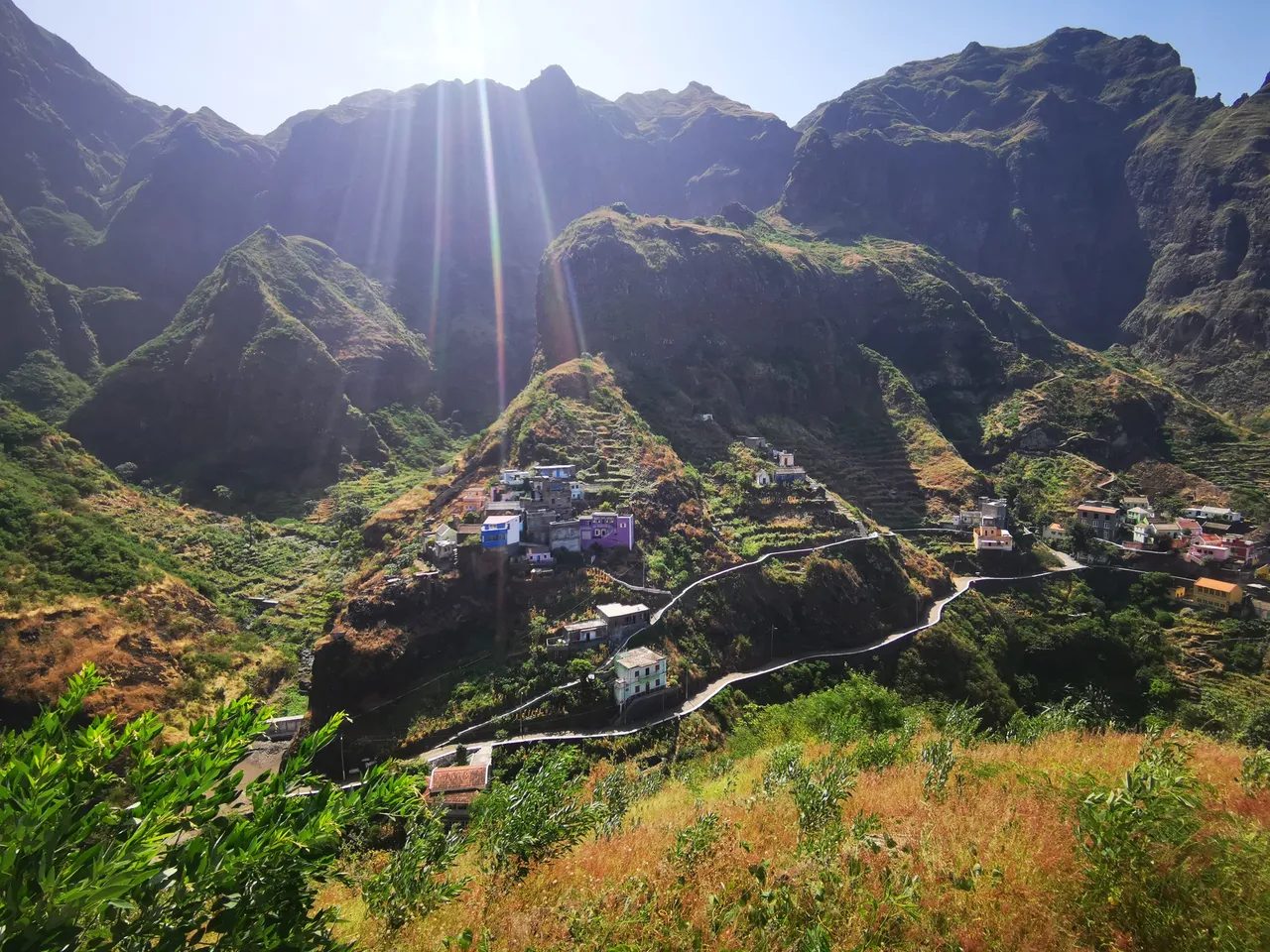 Colourful houses of Fontainhas perched on a green ridge between steep mountains, with a walled path winding below, Santo Antão