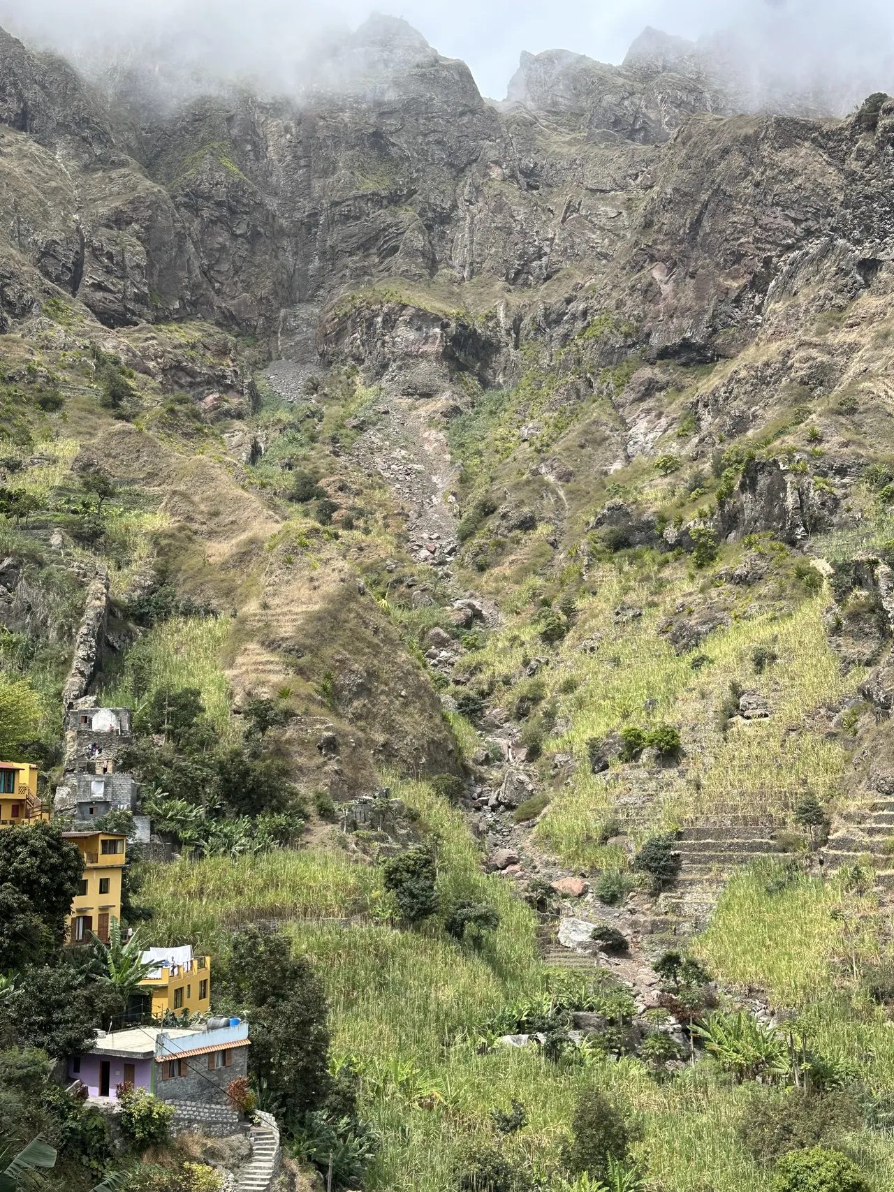Towering rock walls above terraced sugar-cane fields and yellow houses in Ribeira do Paul, Santo Antão